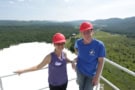 Two people wearing red hard hats stood on a platform overlooking a telescope