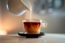 A close-up shot of pouring milk into a cup of hot tea