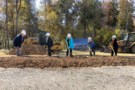 Five people in hard hats hold shovels at a construction site