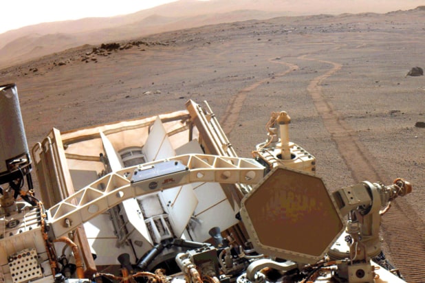 The surface of Mars with wheel tracks in the background and part of the Perseverance Mars rover in the foreground