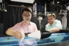 Qiang Zhong holds the swimming robot above a water tank as Dan Quinn looks on